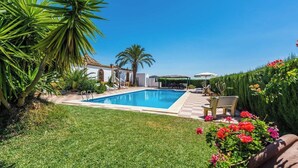 A swimming pool with a checkered deck, surrounded by palm trees and a well-maintained lawn. - Cortijo Hacienda Nueva Lora del Río by Ruralidays (Sevilla)