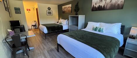 A hotel room with two beds, a desk, a chair, a TV, and a small table.