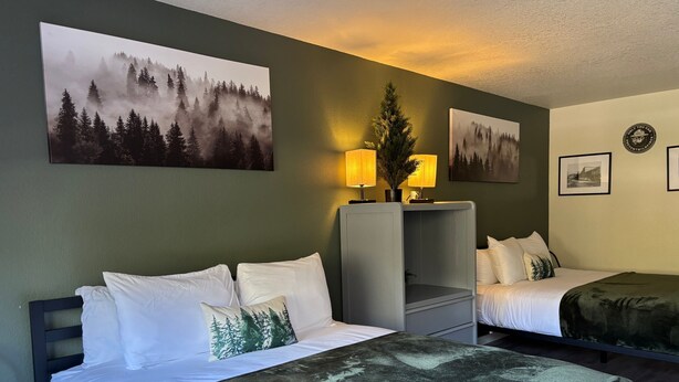 A hotel room with two beds, a nightstand with a lamp, and forest-themed artwork on the walls. - Red Bell Inn (Leavenworth)