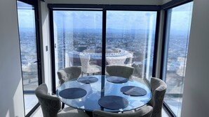 A high-rise room with a glass table and chairs, large windows offering a city view. - The Pearl of the Pacific @ Altomare Condos (Mazatlán)
