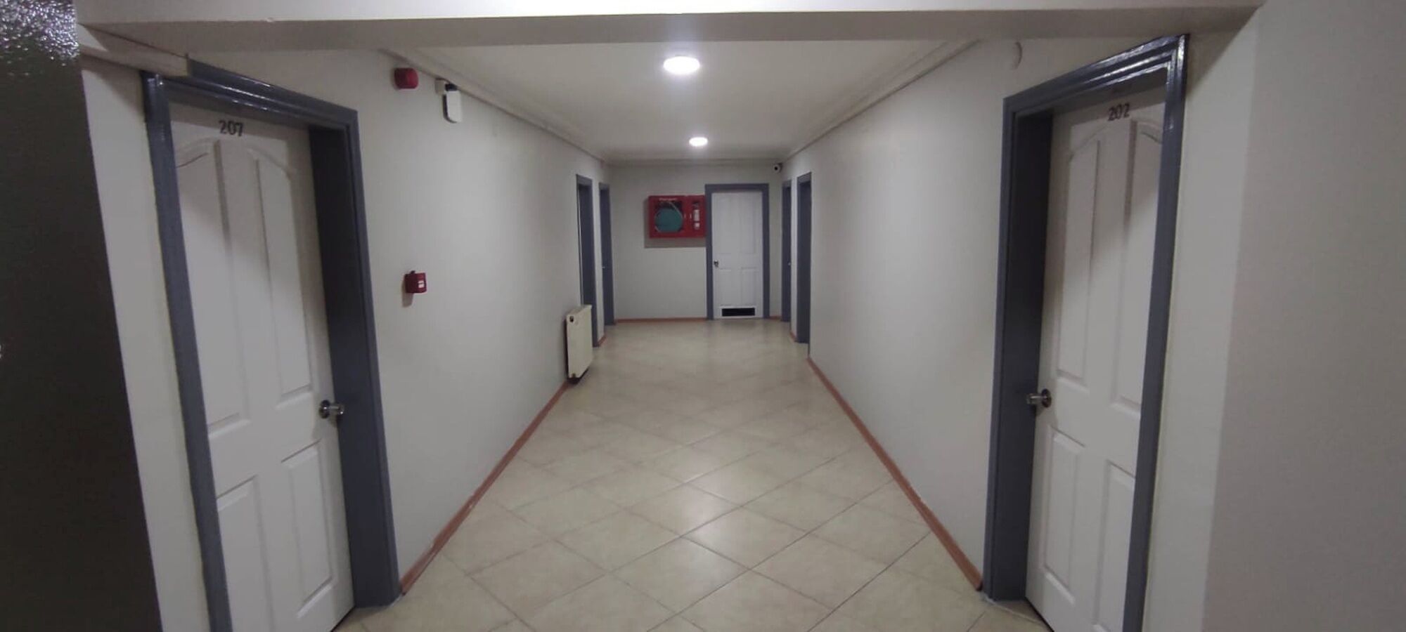 A hallway with white tiled floors and doors on both sides. - DEFNE OTEL  (Polatli)