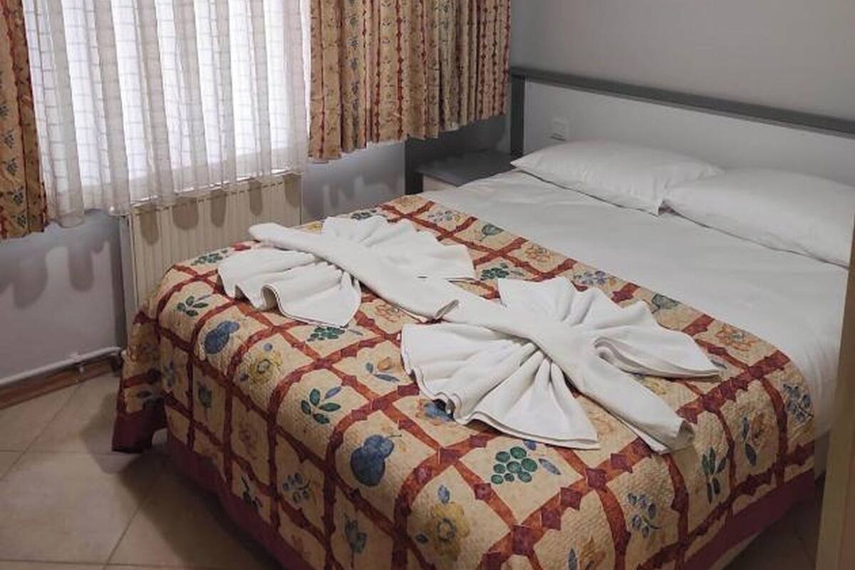 Hotellihuone, jossa on sänky, verhot, patteri ja seinään kiinnitetty valaisin.