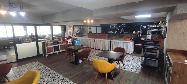A spacious dining area with a high ceiling, a kitchen area with modern appliances, and a seating area with a fireplace. - DEFNE OTEL (Polatli)