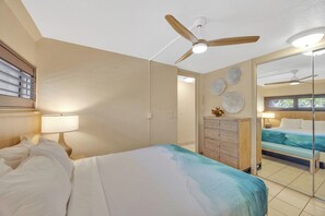 Una habitación de hotel con cama, escritorio, cómoda y ventilador de techo.