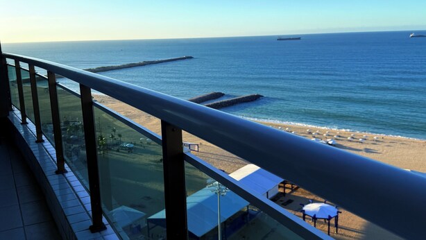A balcony with a view of the beach and ocean, a pier, and beach umbrellas. - Terraços do Atlântico - 2 (Fortaleza)