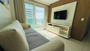 A modern living room with a sofa, TV, and a balcony with a view of buildings. - Terraços do Atlântico - 2 (Fortaleza)