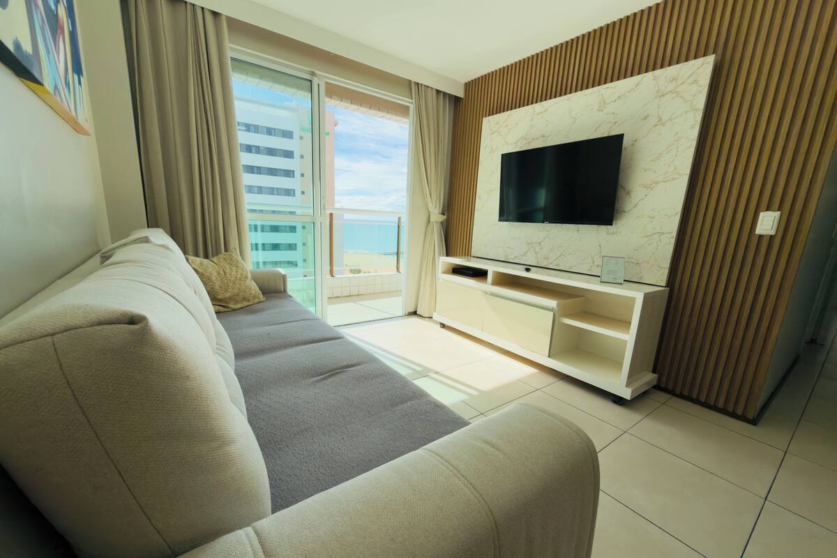 A modern living room with a sofa, TV, and a balcony with a view of buildings.