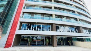 A multi-story hotel with a curved facade, large windows, and a prominent red vertical element. - Terraços do Atlântico - 2 (Fortaleza)