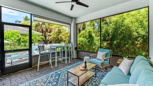 A spacious balcony with a ceiling fan, a seating area with a sofa and chairs, and a view of lush greenery. - 131 Seminole Ln (Cocoa Beach)