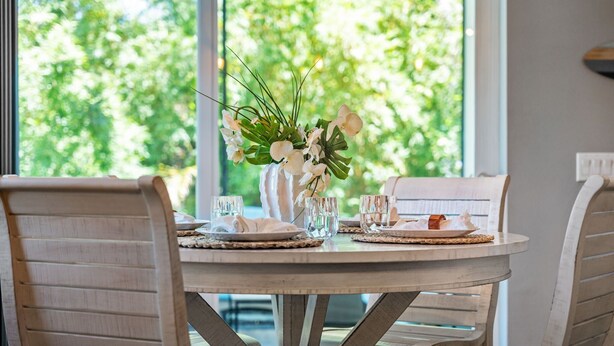 A round dining table with white chairs, a vase with flowers, and glassware set for two. - 131 Seminole Ln (Cocoa Beach)