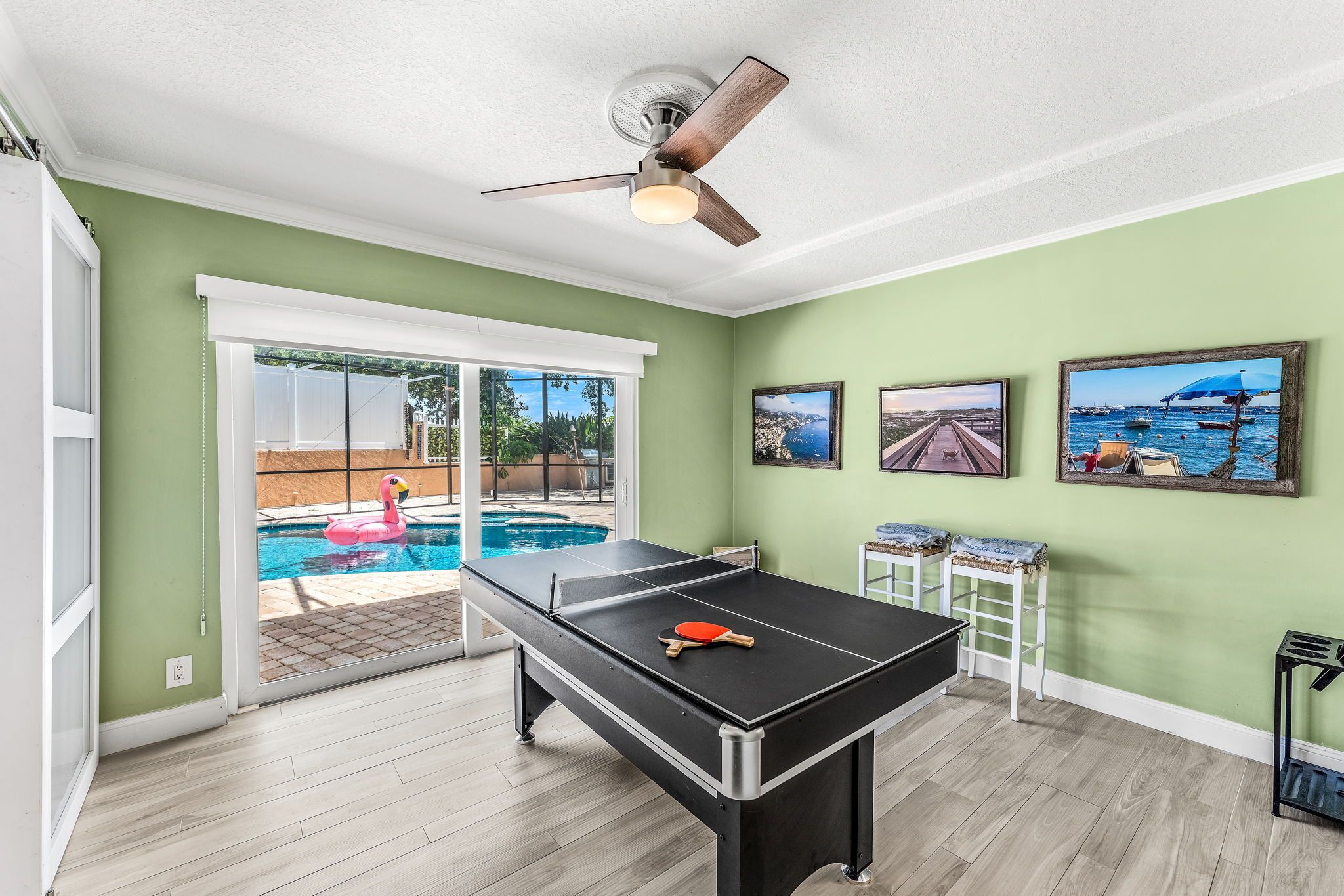 A pool table in a room with green walls, a ceiling fan, and three framed pictures on the wall.