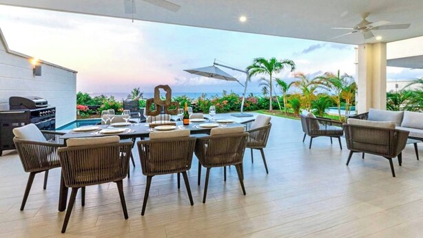 An outdoor dining area with a view of the ocean, surrounded by wicker chairs and a pool. - Villa Ferraj - by Zenbreak (Westmoreland)