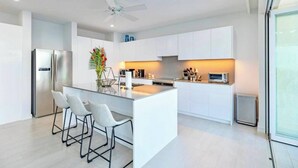A modern kitchen with white cabinetry, a central island with bar stools, a stainless steel refrigerator, and a ceiling fan. - Villa Ferraj - by Zenbreak (Westmoreland)