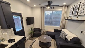 A modern living room with a dark sofa, a round coffee table, and a ceiling fan. - Walkable 1-Bed in East Nash, 2mi to DT, 5 Pts (Nashville)