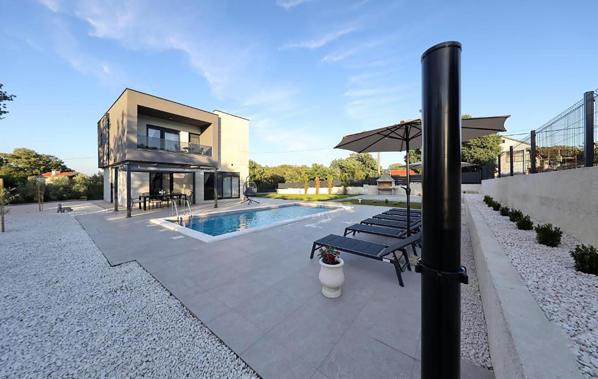 A modern two-story house with a swimming pool, outdoor seating, and a pergola.