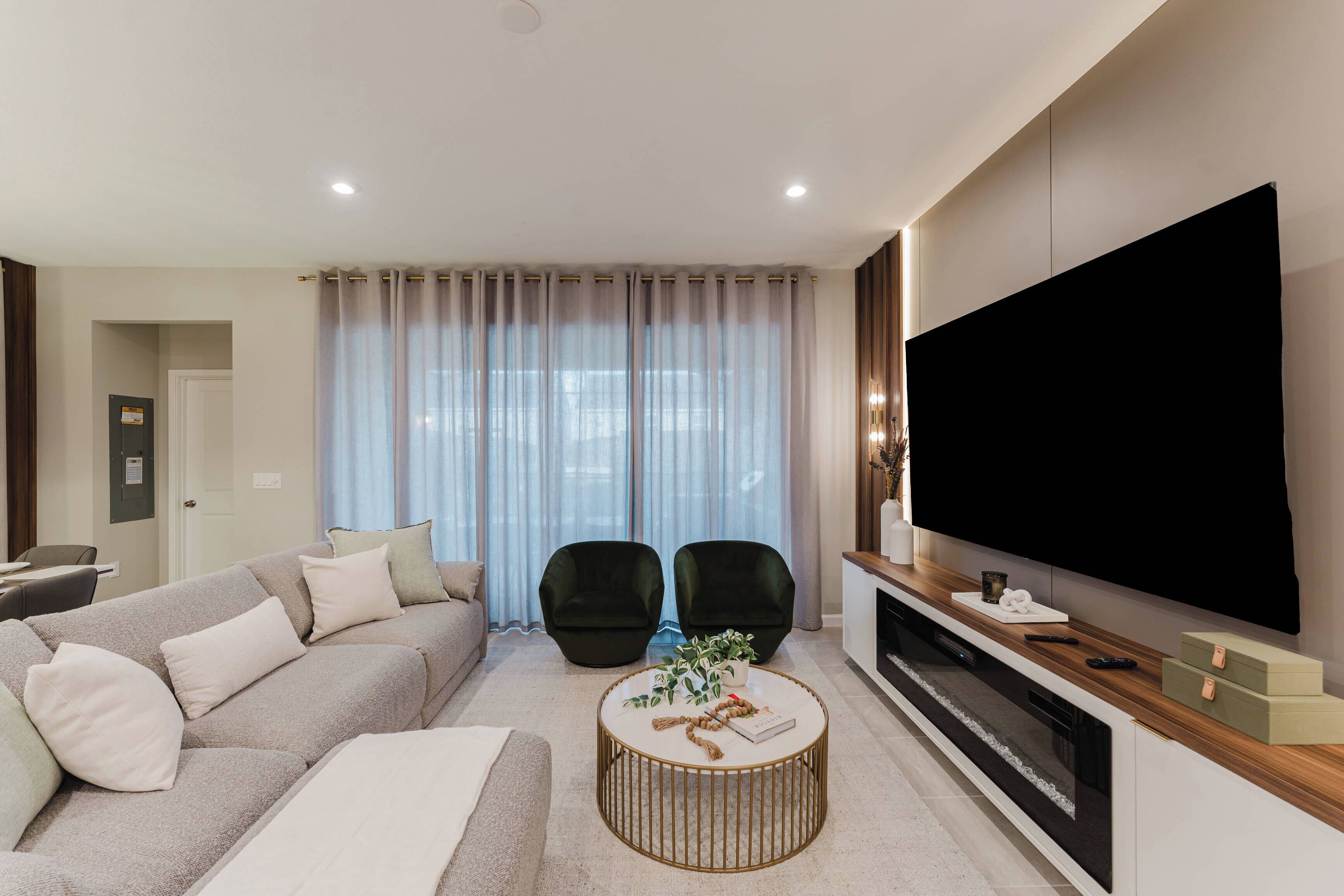 A modern living room with a sofa, two armchairs, a coffee table, and a TV.