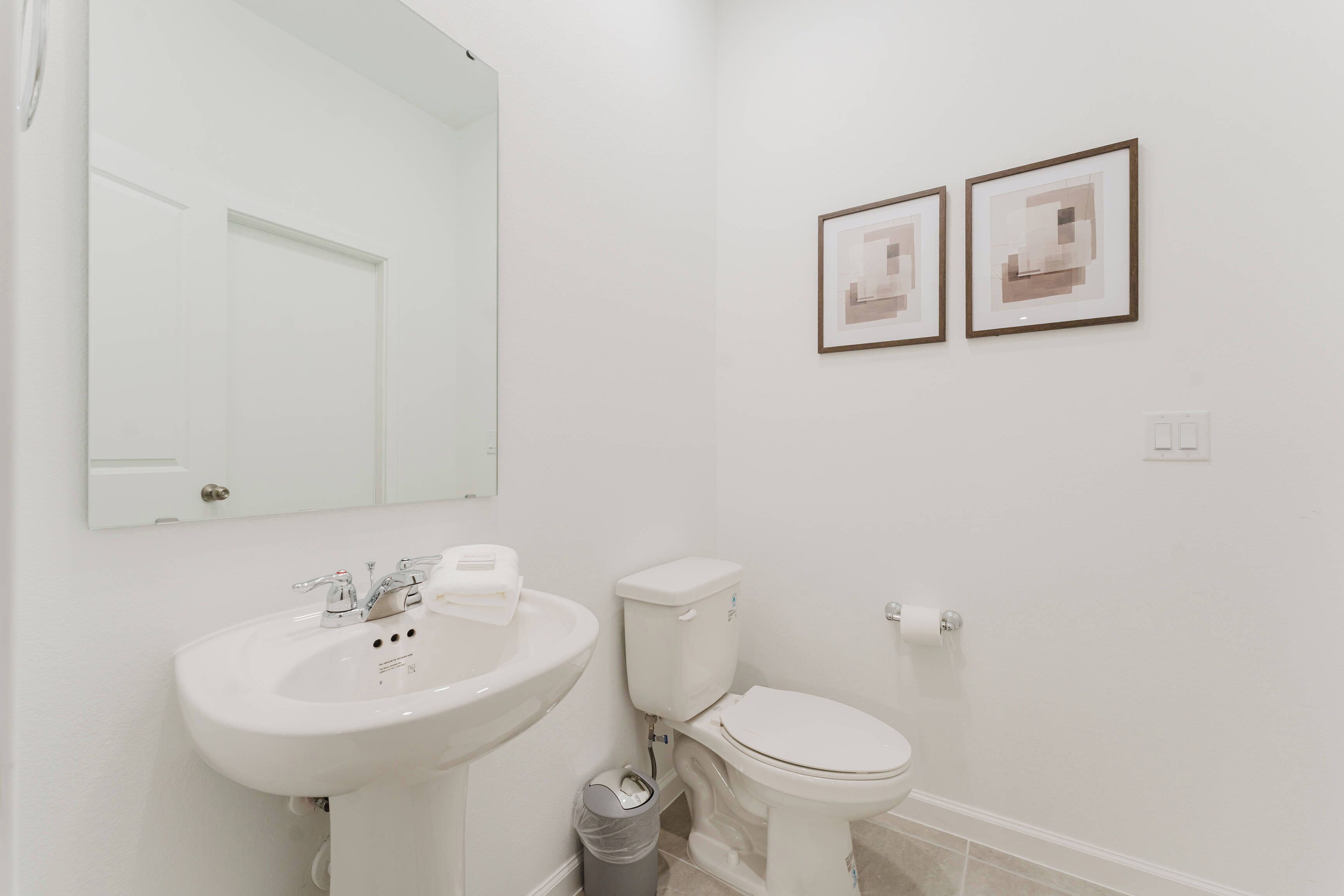 Ein Badezimmer mit einem weißen Waschbecken, einer Toilette und einem Spiegel. An der Wand hängen zwei Bilder in Rahmen.