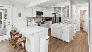 Una cocina moderna con muebles blancos, una isla central con taburetes y vistas al exterior.