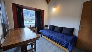 A small room with a wooden table, a sofa bed, and a window with curtains. - Beautiful Large Cabin – Perfect Location & Stunning Views (El Chalten)
