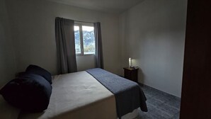 A bedroom with a bed, a nightstand, a lamp, and a window with curtains. - Beautiful Large Cabin – Perfect Location & Stunning Views (El Chalten)