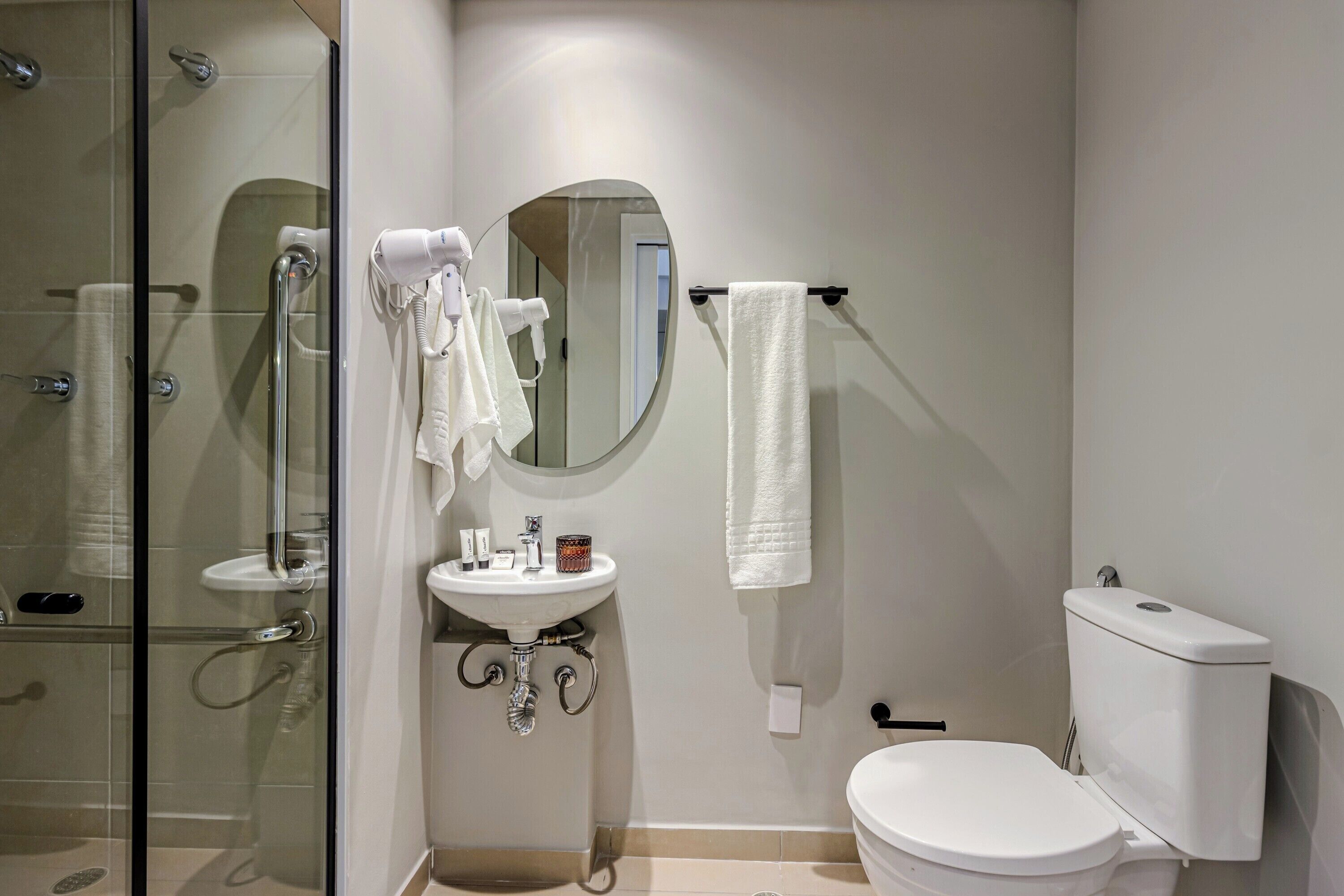 Un baño moderno con cabina de ducha de vidrio, lavamanos blanco, espejo redondo y un inodoro.