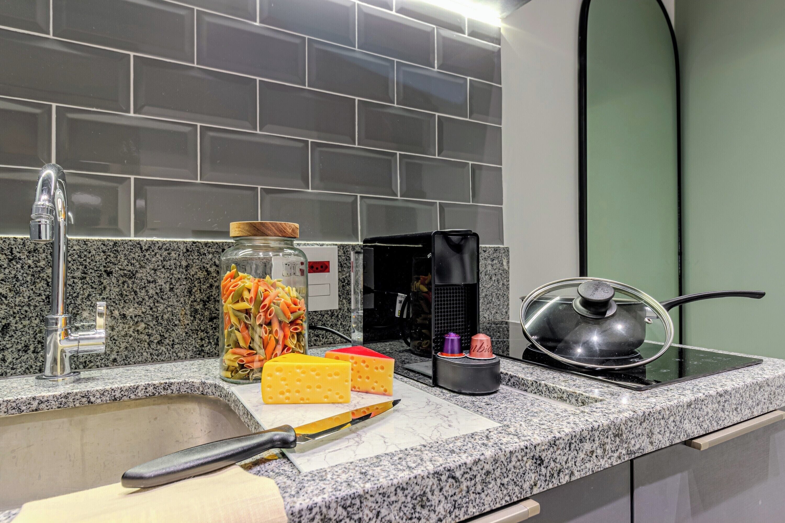 Eine Küche mit Granit Arbeitsplatte, einem Spülbecken, einer Kaffeemaschine, einem Topf auf dem Herd und einem Glas mit Pasta.
