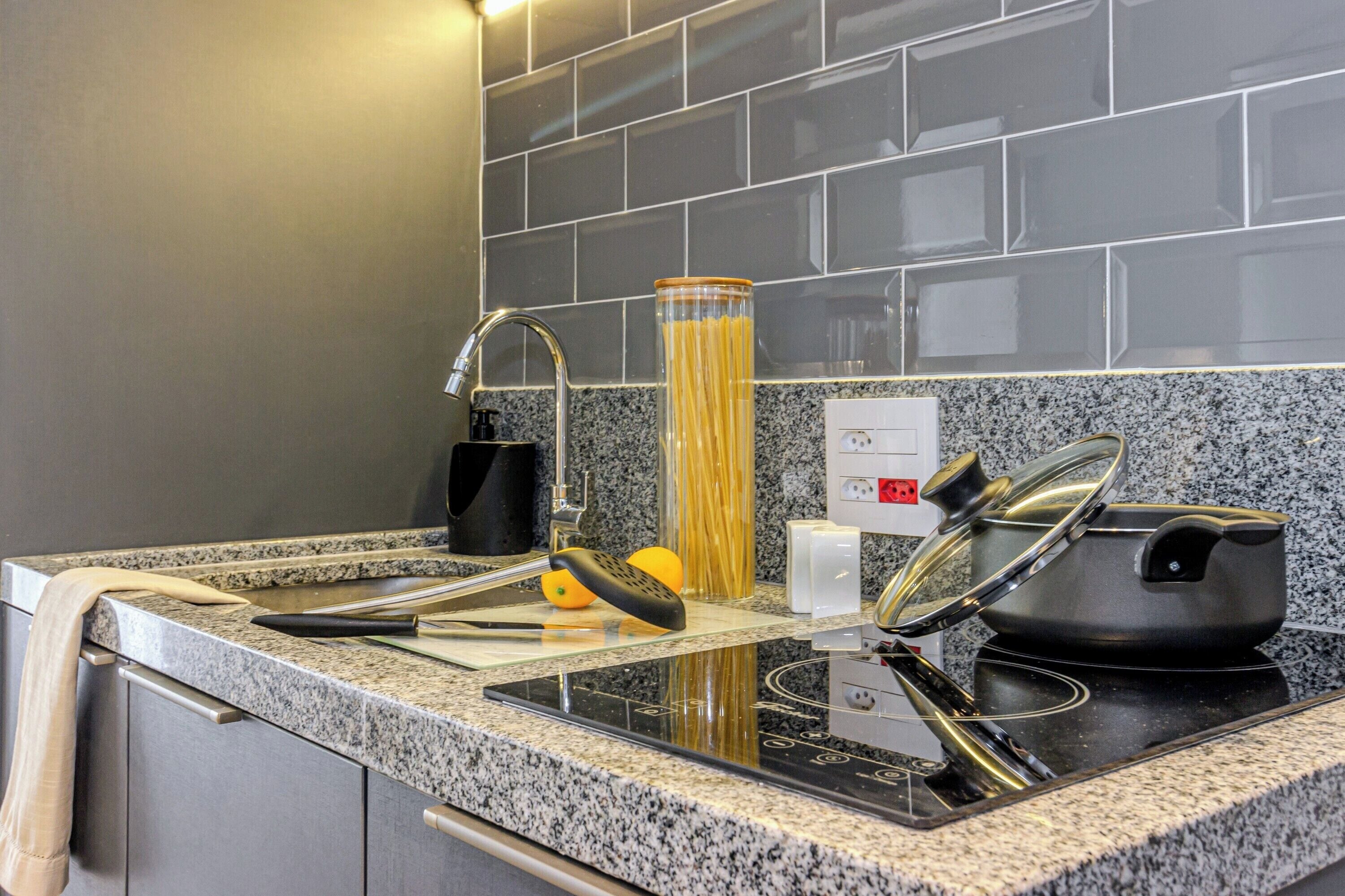 Una cocina con encimeras de granito, un lavamanos de acero inoxidable y una olla negra sobre una placa de inducción.