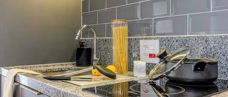 Una cocina con encimeras de granito, un lavamanos de acero inoxidable y una olla negra sobre una placa de inducción.