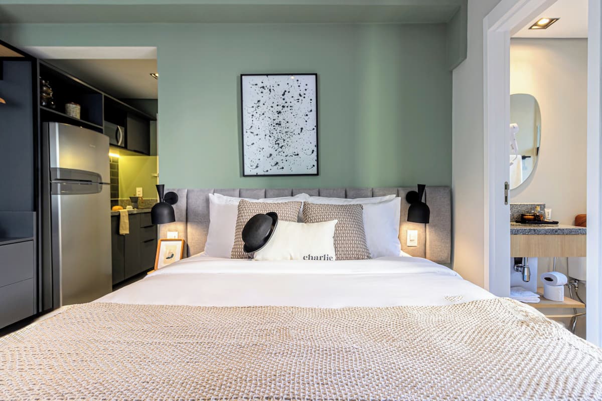 Une chambre d’hôtel moderne dotée d’un grand lit, d’une kitchenette, d’une salle de bain avec un miroir et d’une œuvre d’art encadrée au mur.