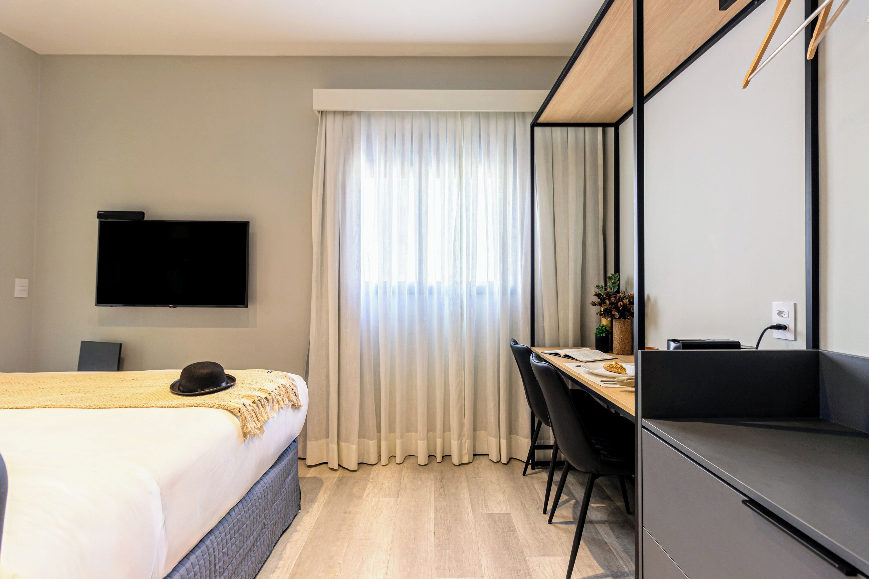 A hotel room with a bed, a desk, a chair, a TV, and a window with curtains.