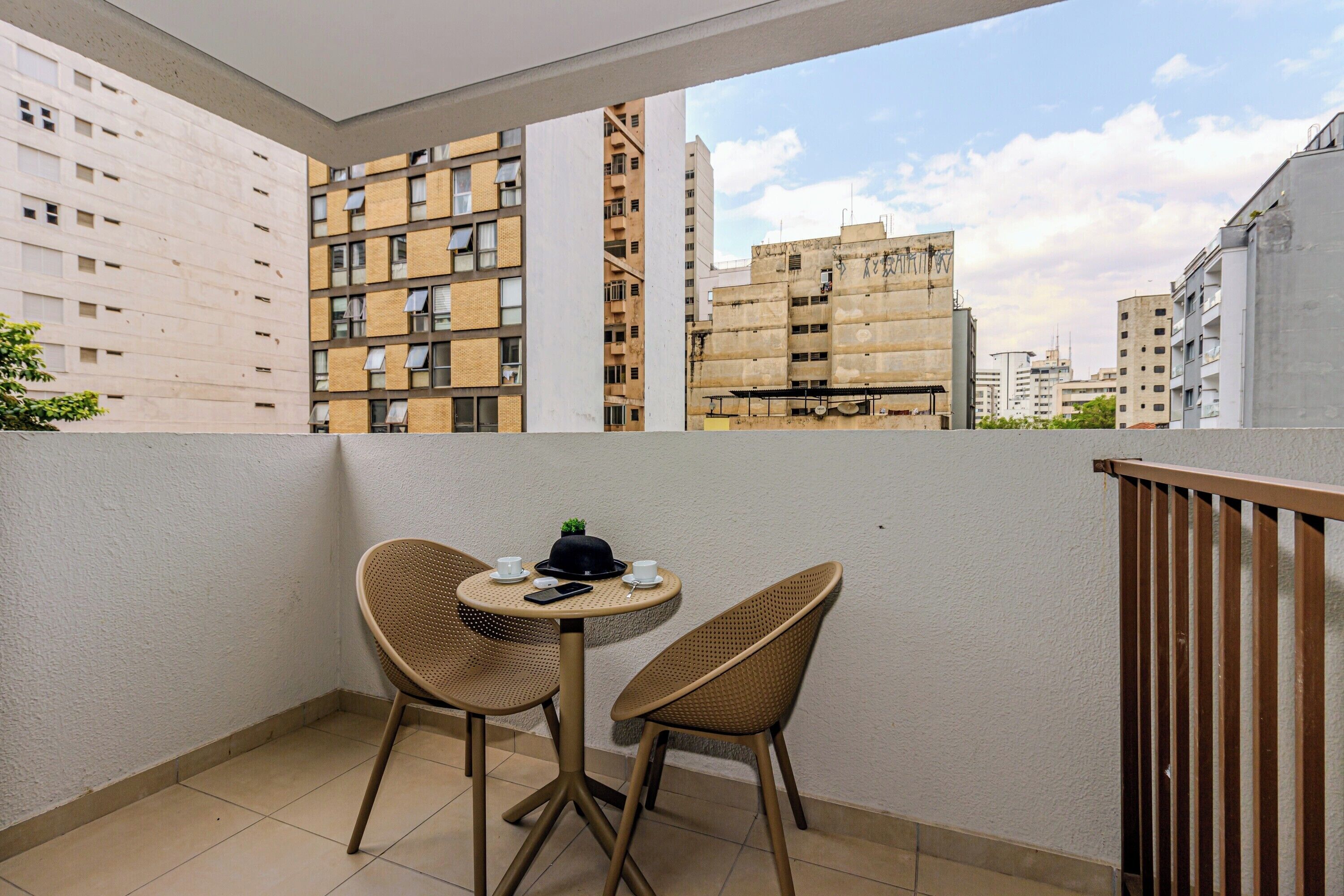 Ein Balkon mit zwei Korbstühlen und einem kleinen runden Tisch, mit Blick auf eine Skyline mit Hochhäusern.