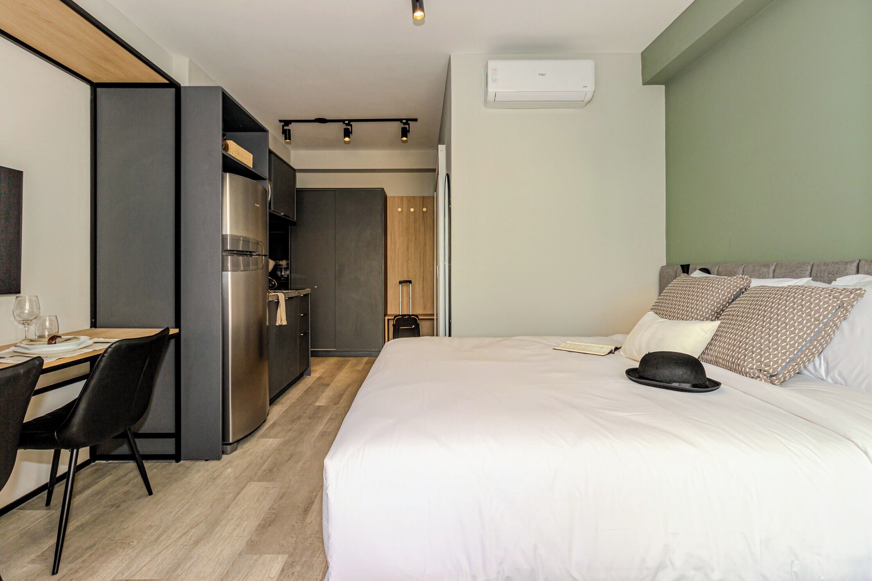Quarto de hotel com cama, escrivaninha, cozinha compacta e banheiro.