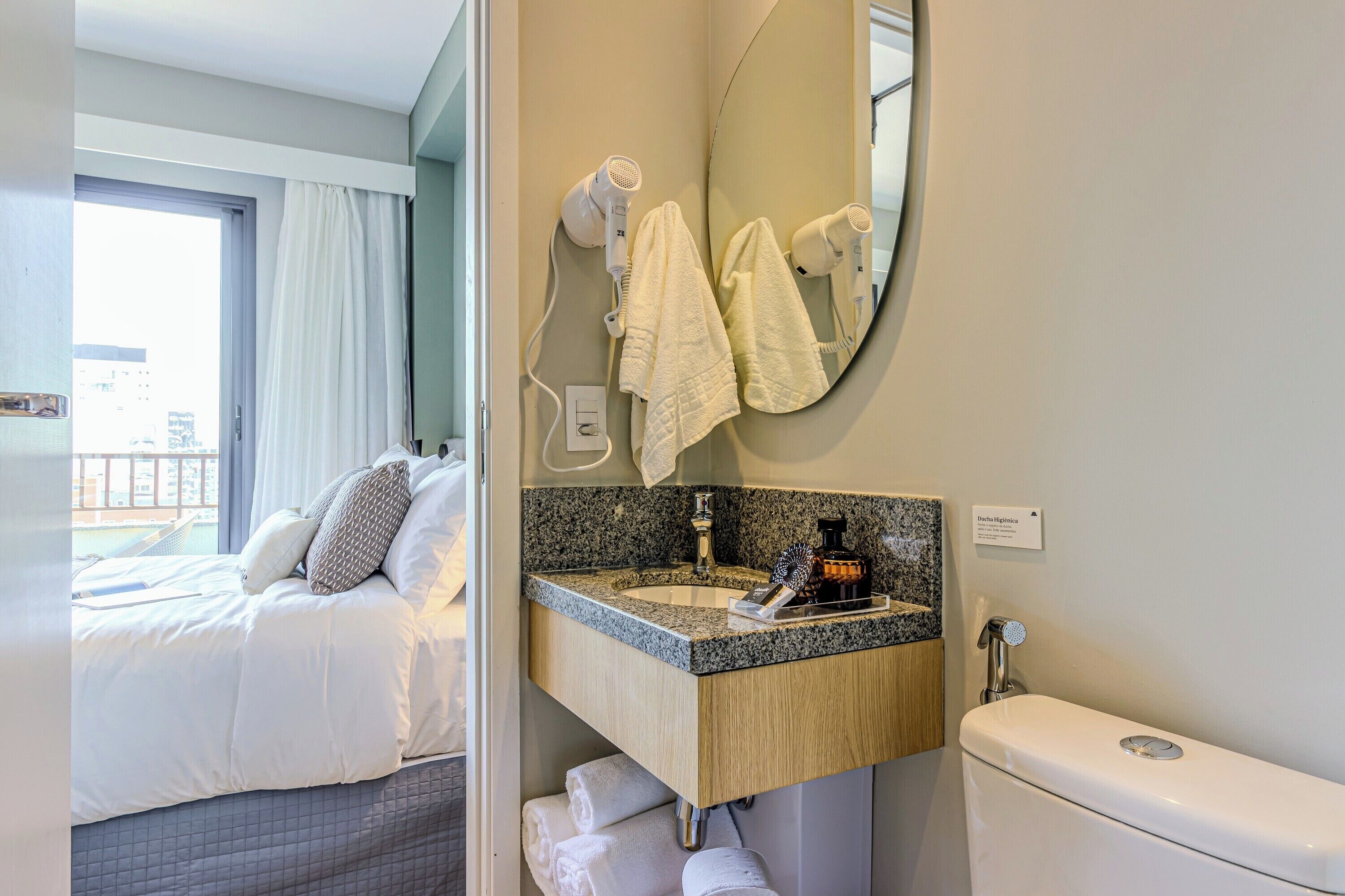 A hotel room with a bed, a bathroom with a sink, a mirror, and towels.
