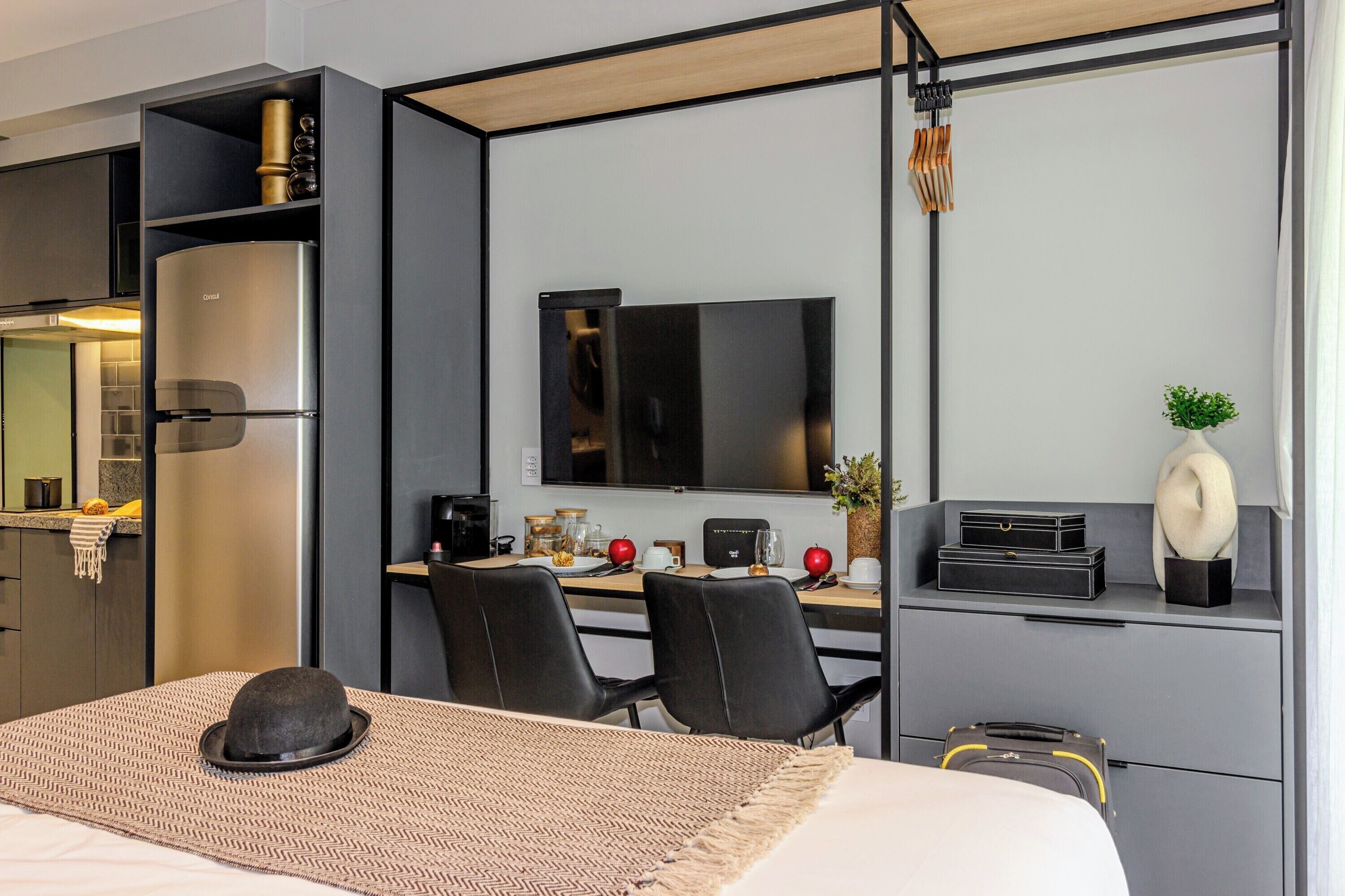 Ein modernes Hotelzimmer mit Bett, Schreibtisch, Computer, Fernseher und einer Küchenzeile.