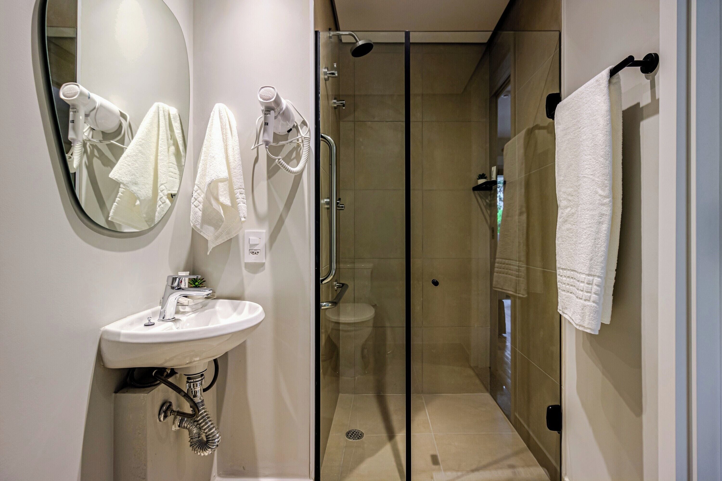 A modern bathroom with a glass-enclosed shower, a sink with a mirror, and two towels hanging on hooks.