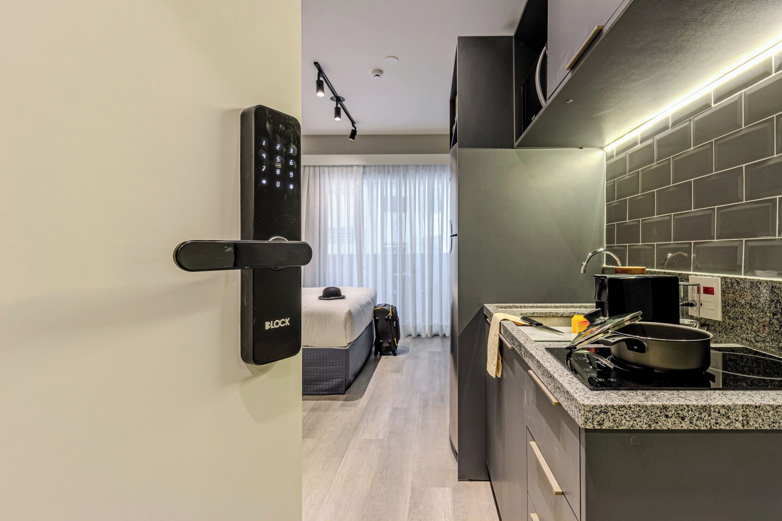 A modern hotel room with a kitchenette, a bed, and a suitcase.