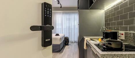 A modern hotel room with a kitchenette, a bed, and a suitcase.