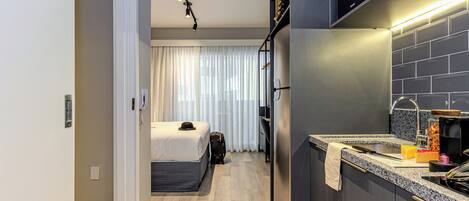 A modern hotel room with a bed, a desk, and a kitchenette.
