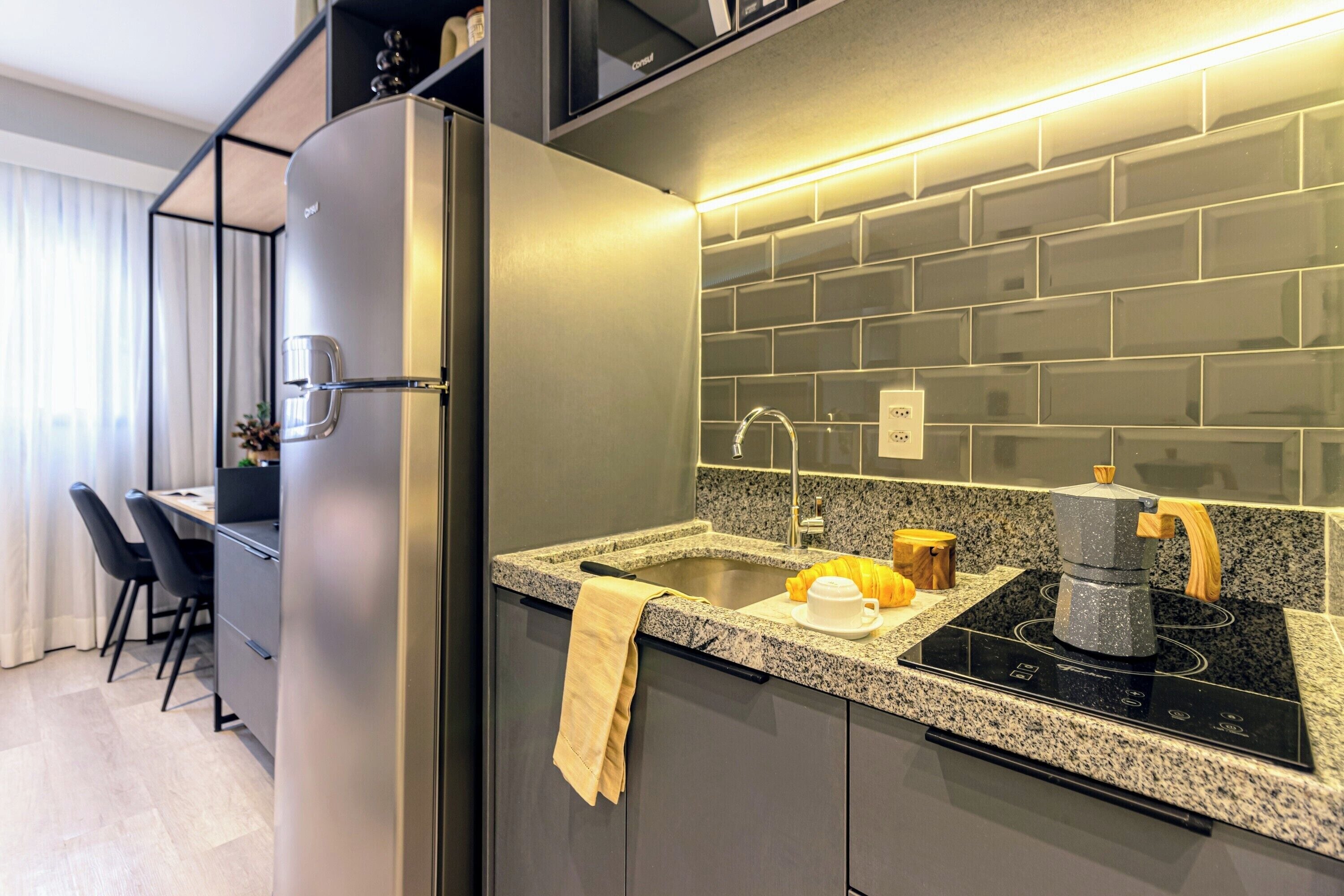 A modern kitchen with a built-in refrigerator, granite countertop, and a coffee machine.