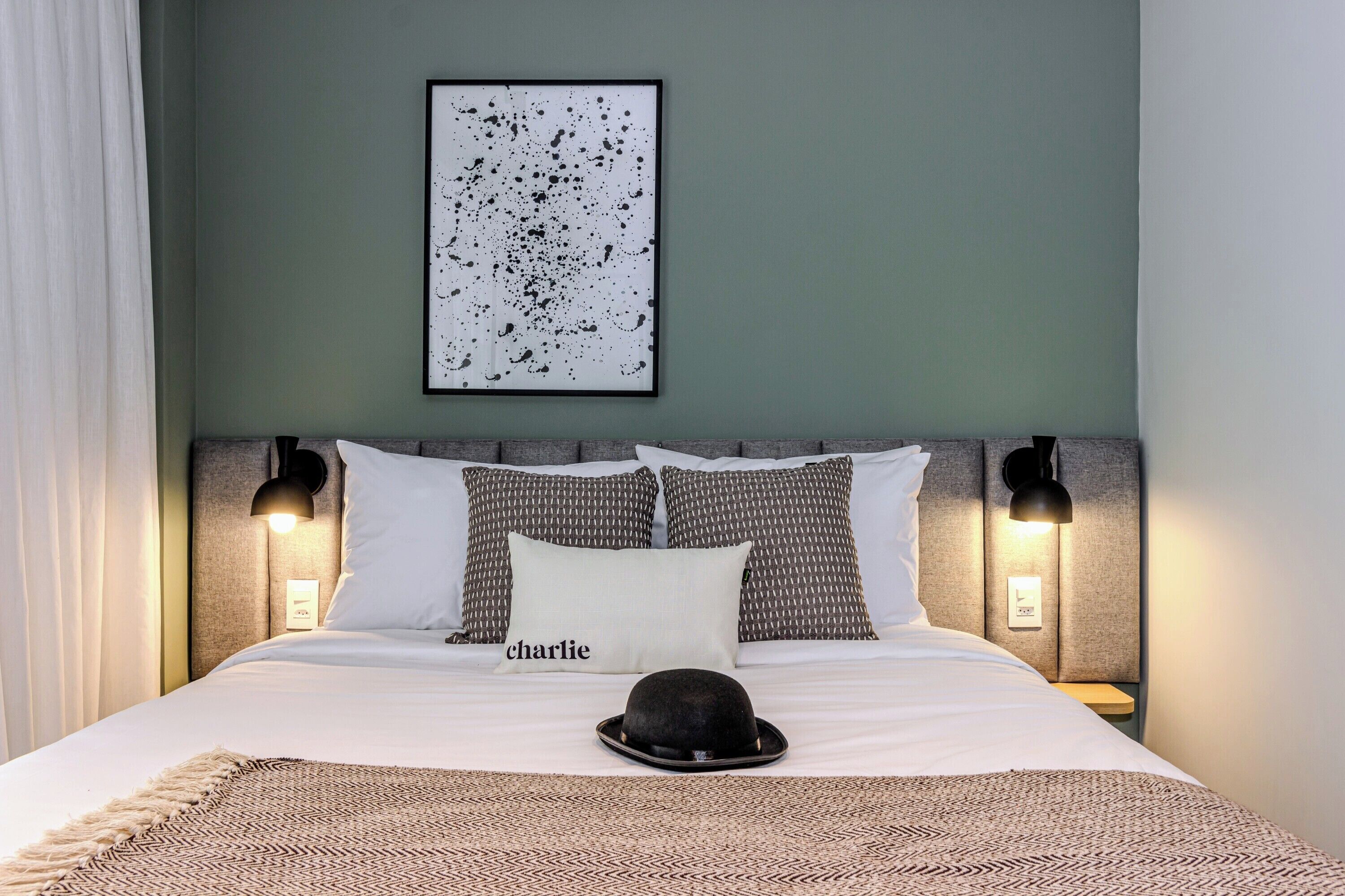 A neatly made bed with a patterned throw, a pillow with the name 'charlie,' and a black hat on the bed.