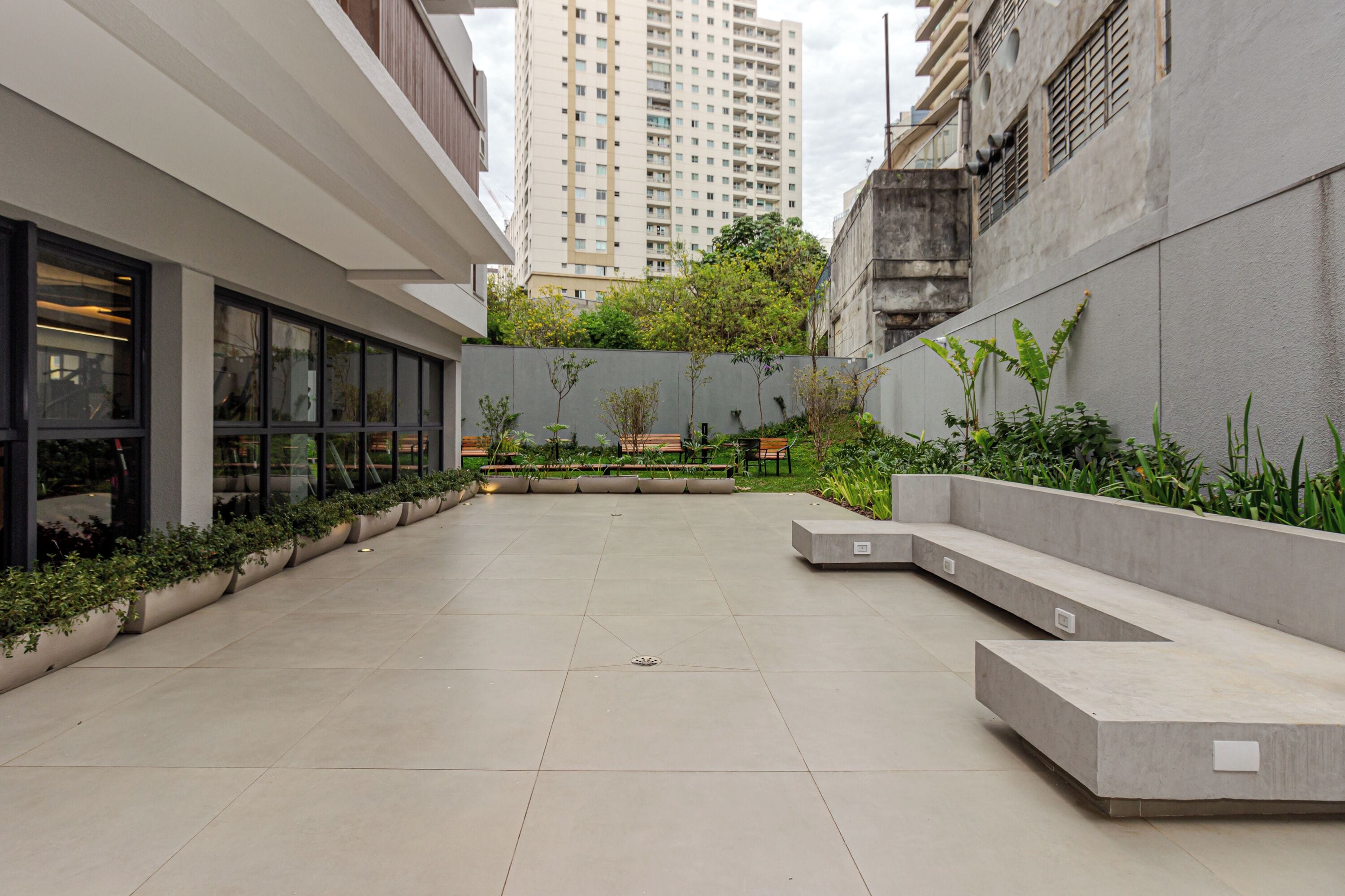 A modern courtyard with a central seating area, surrounded by buildings and greenery.