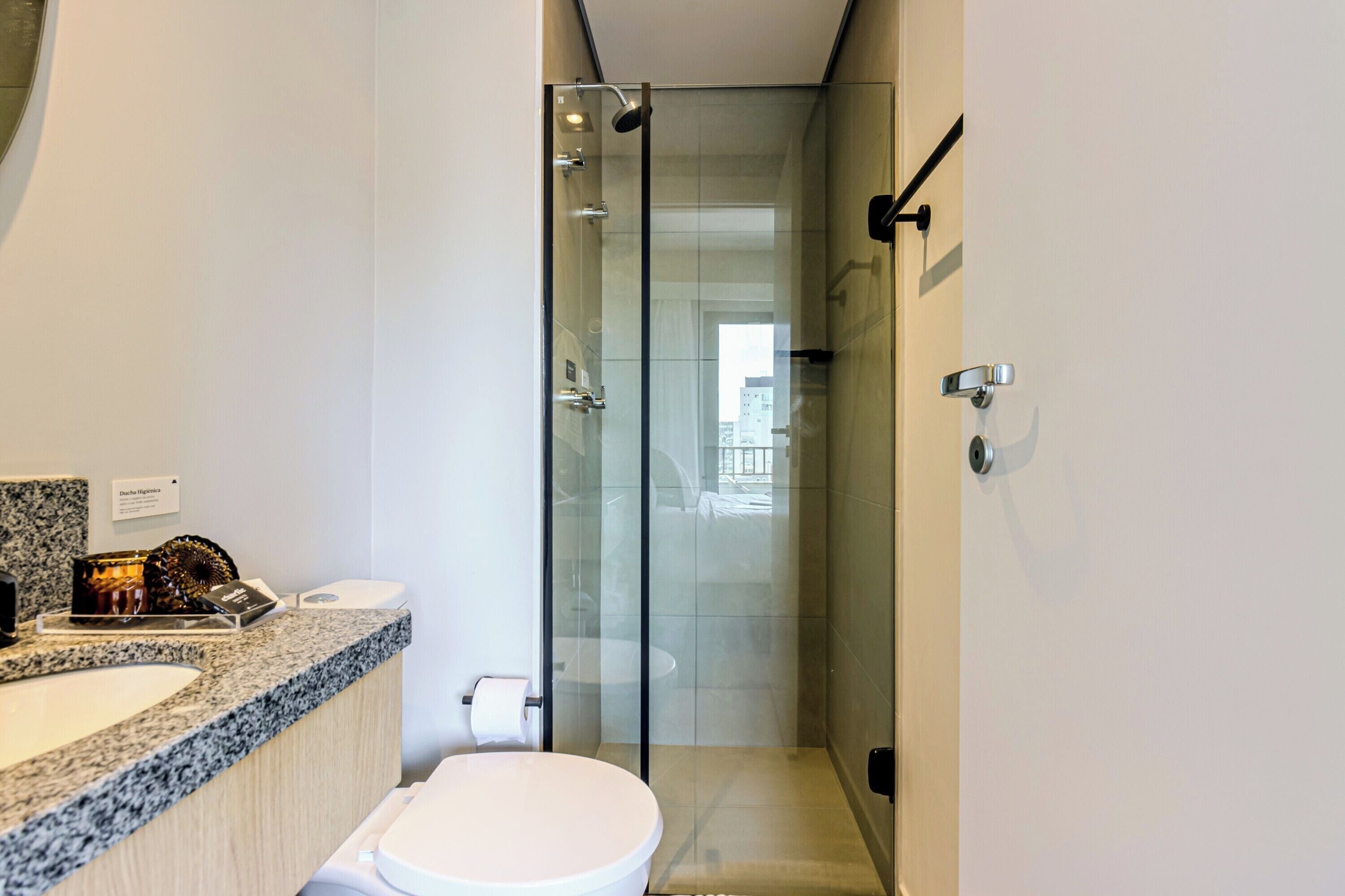 A modern bathroom with a granite countertop, a toilet, and a glass-enclosed shower.