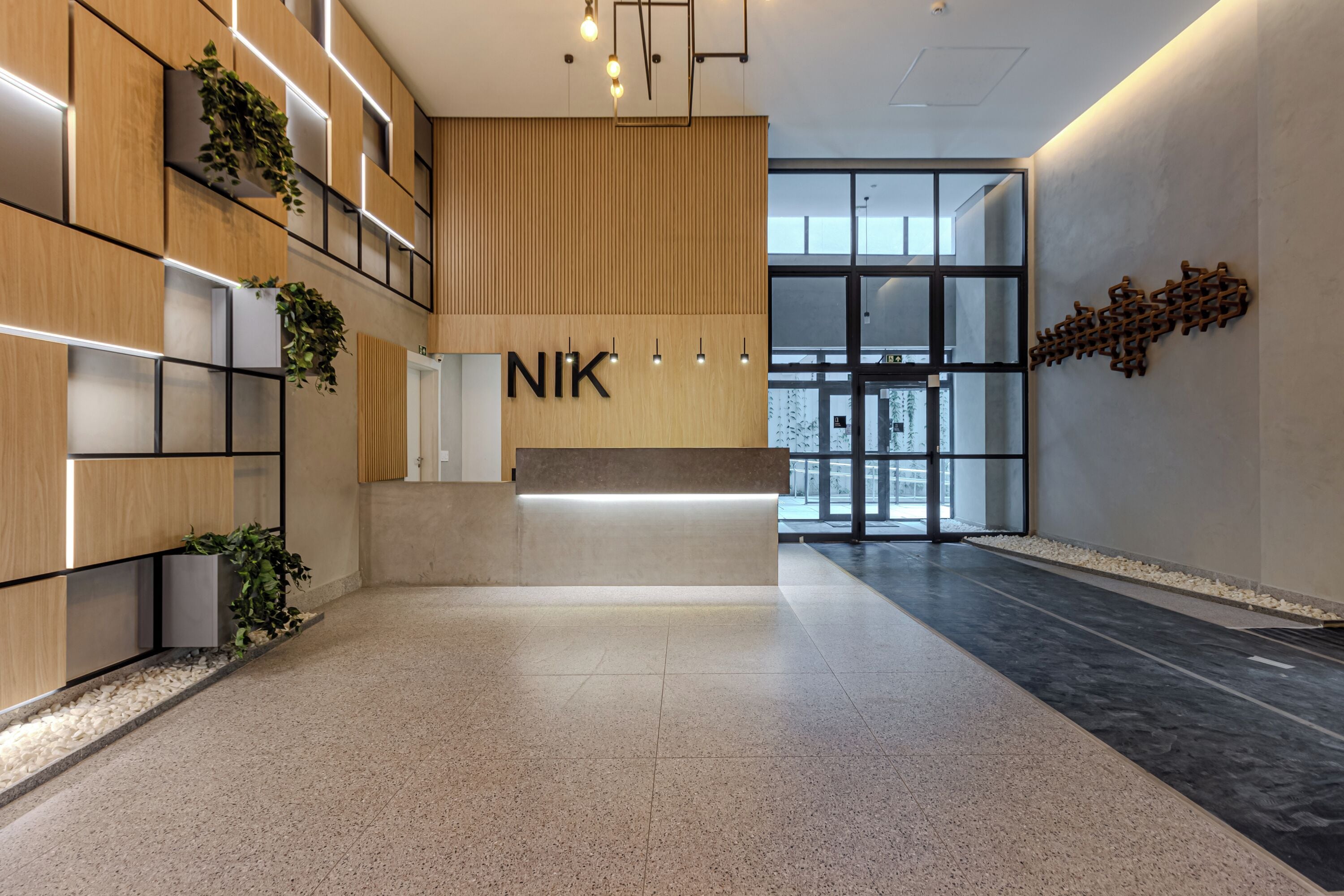 A modern reception area with a wooden reception desk, a large glass door leading outside, and a wall-mounted light fixture.
