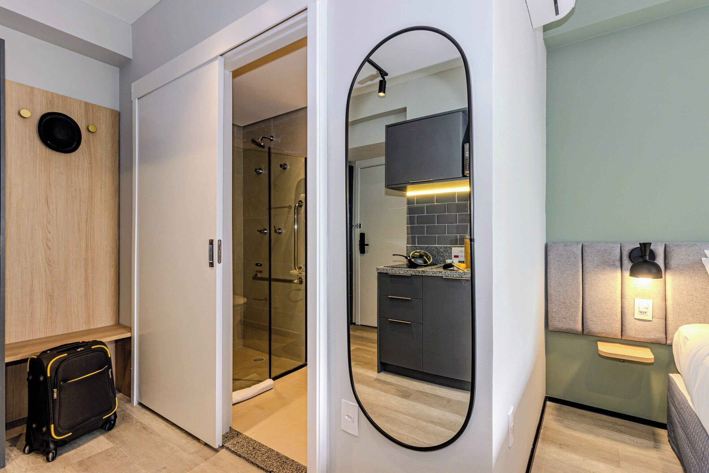Una habitación de hotel moderna con vestidor, ducha de vidrio, zona de cocina y un espejo grande.