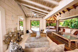 A spacious living area with a high ceiling, wooden beams, a large window with a view of greenery, and a cozy seating arrangement. - Kyalami - by Zenbreak (Holetown)