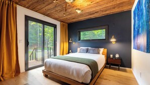 Une chambre avec un plafond en bois, un grand lit, une table de chevet et une fenêtre donnant sur les arbres.