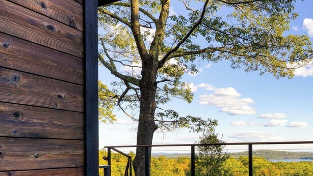 Une terrasse en bois avec un jacuzzi, entourée d’arbres et offrant une vue sur le paysage.