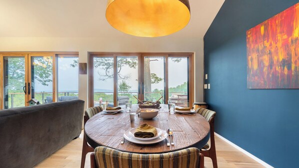 A dining area with a round table, chairs, and a view of the outdoors. - Modern Catskills Escape w/ Open Living, Steam Shower, & Hot Tub w/ Mountain Views, Minutes From Woodstock & Trails Suncliff Vista (Glenford)