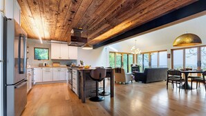 Une cuisine spacieuse avec des poutres apparentes en bois au plafond, un coin repas agrémenté d’une grande fenêtre et une vue sur l’extérieur.