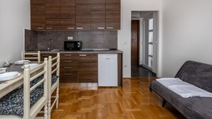 Ett kompakt bostadsutrymme med ett litet kök, trägolv, en matplats med ett vitt bord och stolar samt en grå soffa.